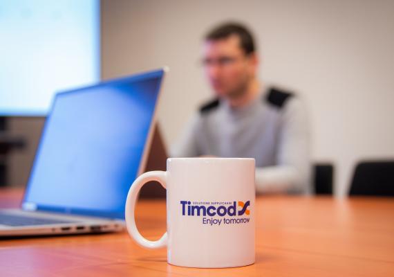 Image d'une tasse avec le logo TIMCOD avec un collaborateur TIMCOD en fond 